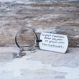 Op de afbeelding: Zilveren sleutelhanger met een stervormige hanger en een hartvormige hanger. Het label heeft de tekst "Un papa formidable donne toujours un grand-père EXCEPTIONNEL."