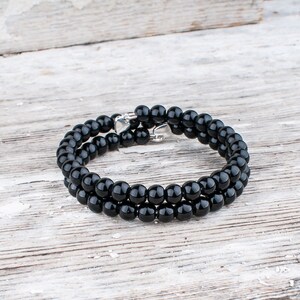 May include: A black beaded bracelet with a silver clasp. The bracelet is made of round, smooth beads and is double-layered.