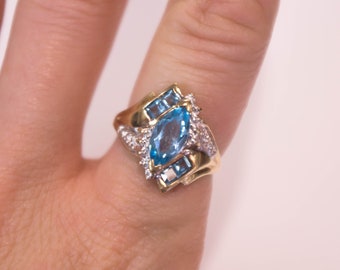 May include: A gold ring with a large blue topaz gemstone surrounded by smaller blue topaz and white diamonds.