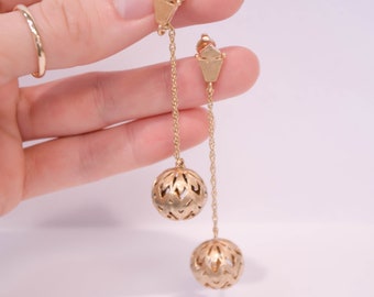 May include: A pair of gold dangle earrings with a delicate chain and a round, openwork ball at the end of each chain.