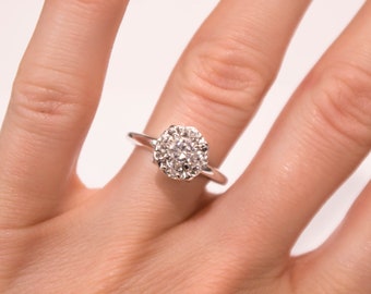 May include: A silver ring with a round, white diamond center stone surrounded by smaller diamonds.
