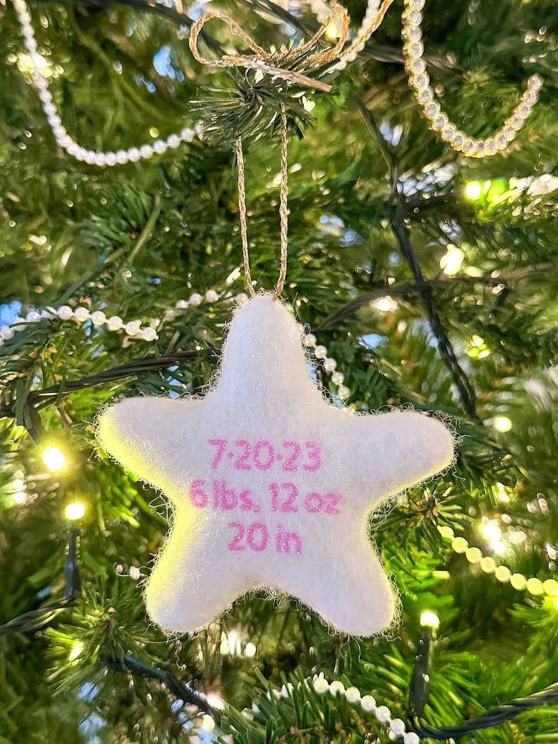 K&ouml;nnte beinhalten: Wei&szlig;er Filzstern-Anh&auml;nger mit rosa Stickerei. Der Anh&auml;nger zeigt "7.20.23 6 lbs, 12 oz 20 in".