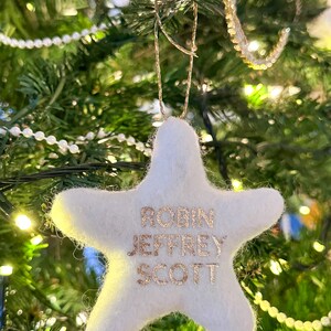 K&ouml;nnte beinhalten: Wei&szlig;er Filzstern-Anh&auml;nger mit goldenen Glitzerbuchstaben, auf dem "Robin Jeffrey Scott" steht, der an einem Weihnachtsbaum h&auml;ngt.