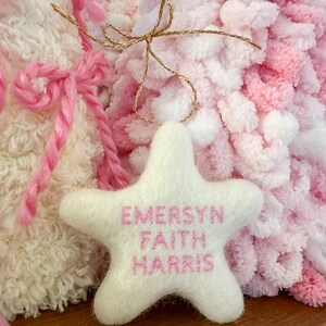 K&ouml;nnte beinhalten: Wei&szlig;er Filzstern-Anh&auml;nger mit rosa gesticktem Text "EMERSYN FAITH HARRIS".