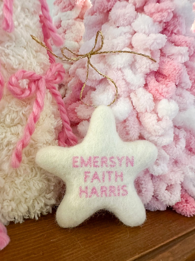 K&ouml;nnte beinhalten: Wei&szlig;er Filzstern-Anh&auml;nger mit rosa gesticktem Text "EMERSYN FAITH HARRIS".