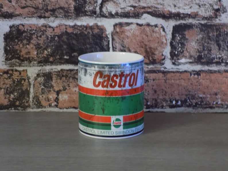 May include: A white ceramic mug with a distressed metal design featuring the Castrol logo in red and white. The mug has a green and red stripe design and the text "Castrol Limited Swindon England".