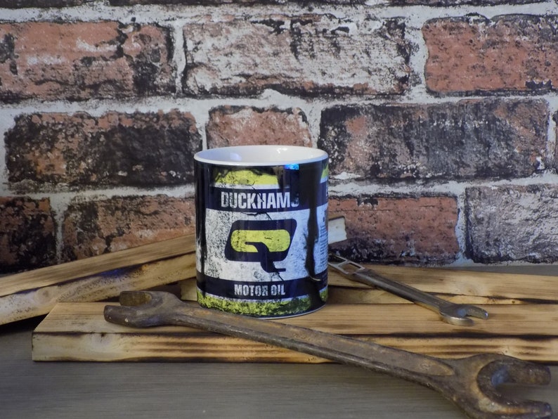 May include: A black ceramic mug with a yellow and white graphic of a vintage motor oil can. The can has the text "Duckhams Motor Oil" on it.