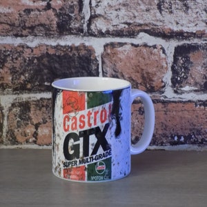 May include: White ceramic mug with a vintage Castrol GTX Super Multi-Grade motor oil can design. The design features a red, green, and black color scheme with a distressed look.