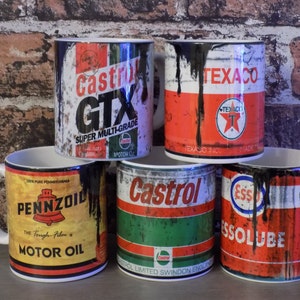 May include: Five vintage-style ceramic mugs with oil can designs. The mugs feature the logos of Castrol GTX, Texaco, Pennzoil, Castrol, and Esso. The mugs are all in different colors and have a distressed look.