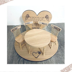 May include: A wooden table setting with three chairs and a heart-shaped plaque with the text "Our loved ones who are unable to be here in person today. We know you will look down on us in our Special Place. If you were with us the thought of you makes our day complete." The chairs are labeled "Dad", "Scott", "Mom", and "Robert".