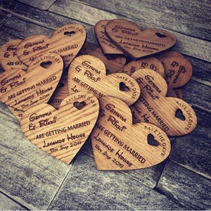 May include: Wooden heart-shaped save the date cards with the text "Gemma & Rikki are getting married" and the date "13th June 2019". The cards are decorated with a small hole at the top and the words "Lemonade House" are printed below the date.