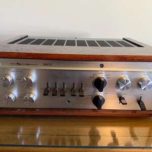 May include: Vintage silver and wood Luxman 38FD stereo receiver. The face has multiple knobs, switches, and inputs. The top has a black vent. The wood frame surrounds the silver face. The model number 38FD is visible.