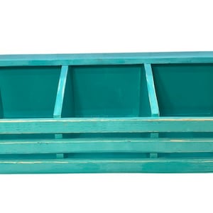 May include: Teal blue wooden box with three compartments and a hinged lid. The box has a slatted front.