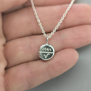 Può includere: Collana d'argento con un ciondolo a forma di pillola inciso con il numero 2064 e un simbolo.
