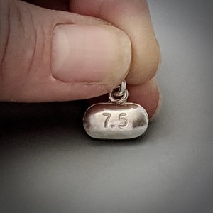 Peut inclure: Un charme en argent en forme de pilule avec le numéro 7,5 gravé dessus.