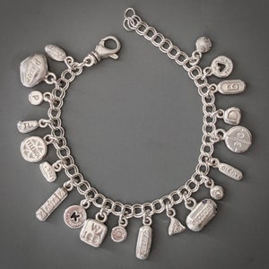 May include: A silver charm bracelet with various charms, including pills, a heart, and a cross. The charms are engraved with text, including "Tylenol", "Micodin", "100", and "30".