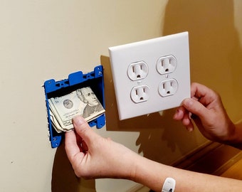 May include: A white electrical outlet cover with four outlets is mounted on a wall. A hand is holding the cover while another hand is placing cash into a blue plastic electrical box behind the cover.