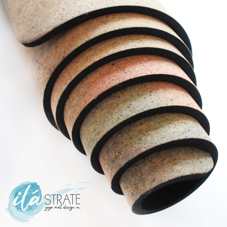 K&ouml;nnte beinhalten: Ein Stapel Kork-Yogamatten mit schwarzen Kanten. Die Matten sind aufgerollt und die oberste Matte ist teilweise abgerollt. Die Matten sind in verschiedenen Braunt&ouml;nen und Beige gehalten. Der Text "it&aacute; STRATE yoga mat design co." ist in der linken unteren Ecke des Bildes zu sehen.