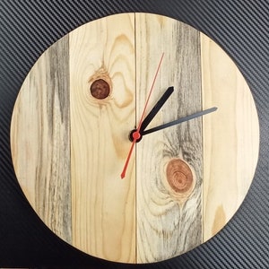 Puede incluir: Un reloj de madera redondo con veta de madera marrón claro y una aguja de segundos roja y agujas de horas y minutos negras.