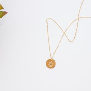 Puede incluir: Un collar de cadena dorada con un colgante redondo con un dise&ntilde;o de espiral.