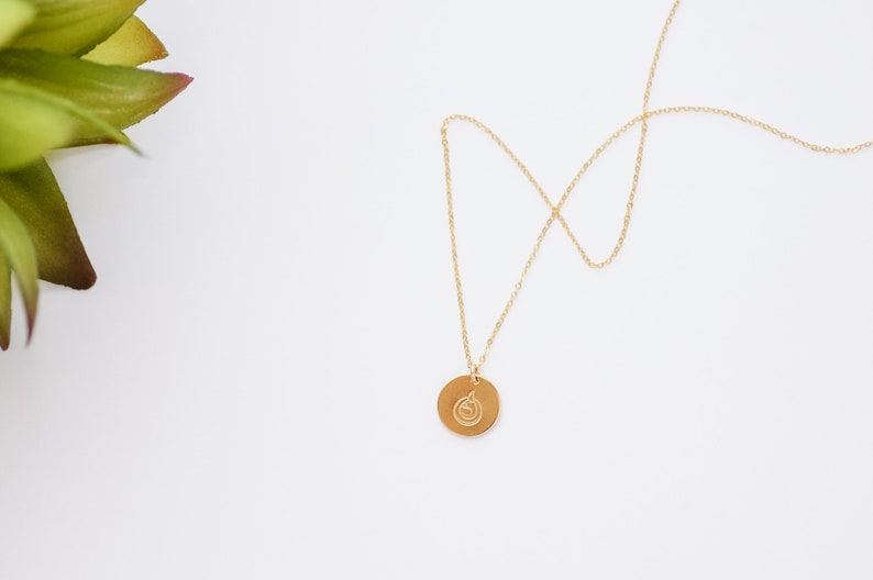 Puede incluir: Un collar de cadena dorada con un colgante redondo con un dise&ntilde;o de espiral.