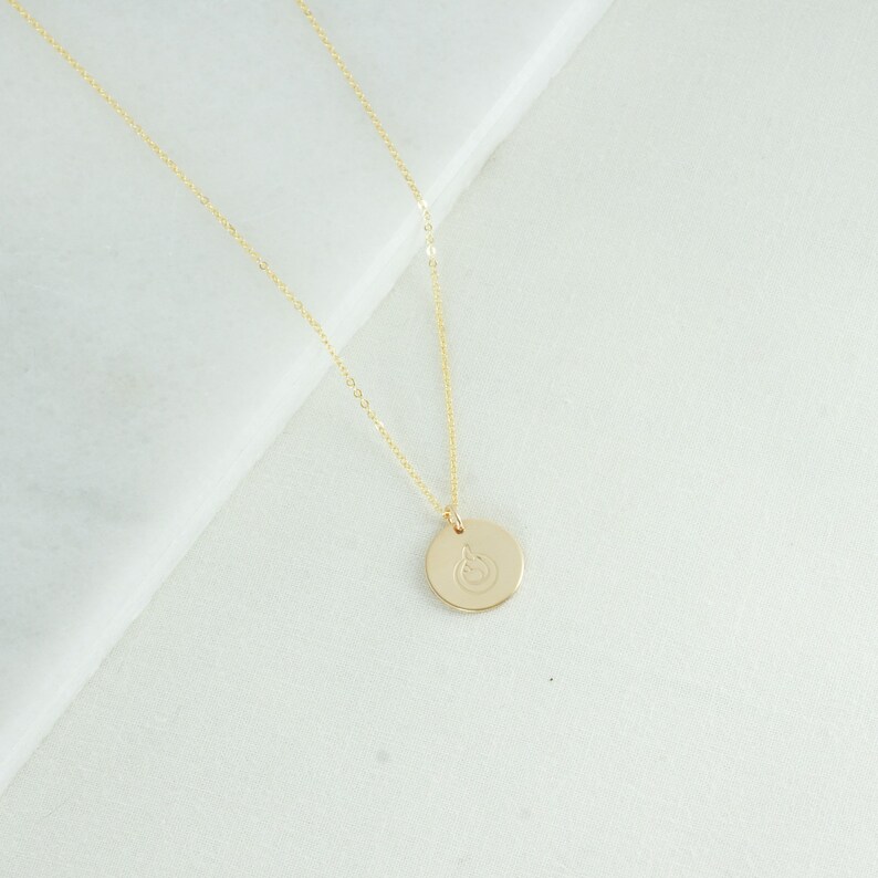 Puede incluir: Un collar de cadena de oro con un colgante redondo que presenta un peque&ntilde;o dise&ntilde;o grabado.