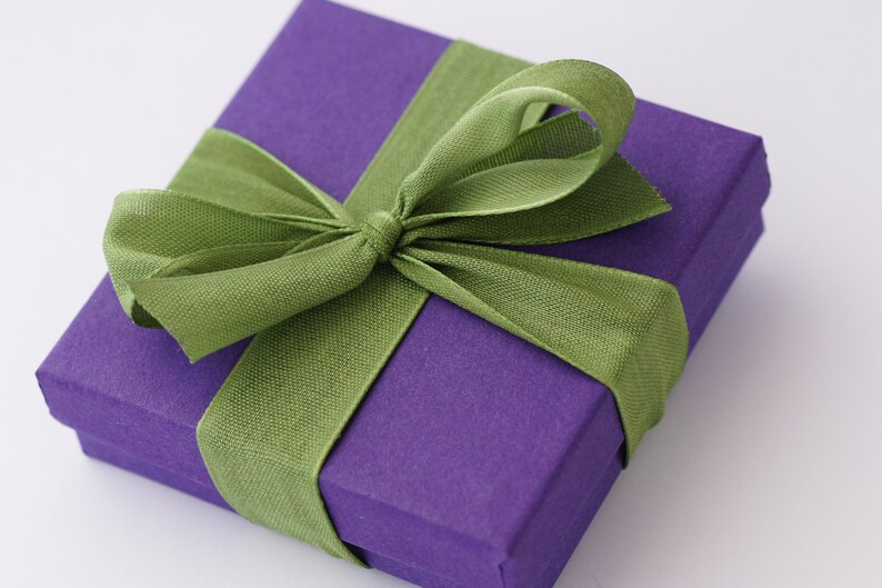 Puede incluir: Una caja de regalo morada con una cinta de sat&eacute;n verde atada en un lazo.