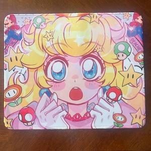 Puede incluir: Una alfombrilla de ratón rosa y amarilla con una imagen de dibujos animados de un personaje con cabello rubio y ojos azules. El personaje está rodeado de estrellas, champiñones y otras imágenes con temática de videojuegos. El texto "PEACHIE" es visible en la esquina superior derecha.