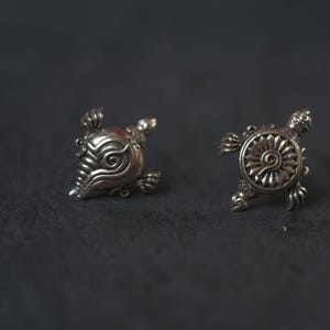May include: Two silver turtle-shaped charms with intricate designs. The charms are on a black background.