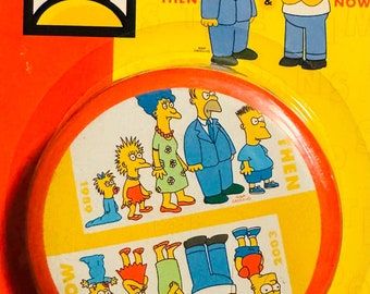 May include: A round, yellow and red coaster with a picture of the Simpsons family. The coaster shows the family in 1989 and 2003. The text "The Simpsons 300th Episode" is on the top of the coaster.
