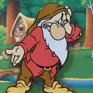 Può includere: Immagine di un cartone animato di Brontolo di Biancaneve. Il personaggio indossa una camicia rossa, pantaloni marroni e scarpe gialle. Ha una barba bianca e un'espressione scontrosa, con la mano sulla fronte. Lo sfondo mostra una foresta e una casetta.