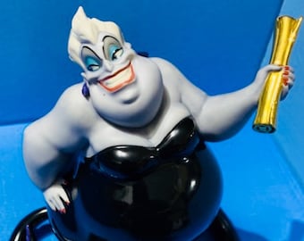 Può includere: Una statuetta di Ursula, personaggio de La Sirenetta Disney, in viola e nero. Tiene in mano un rotolo dorato e ha un'espressione maliziosa sul viso.