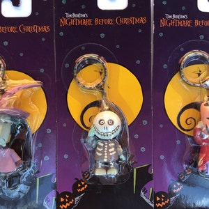 Puede incluir: Tres llaveros de Pesadilla Antes de Navidad con Jack Skellington, Sally y Oogie Boogie. Cada llavero está empaquetado en una tarjeta morada y amarilla con el título de la película.
