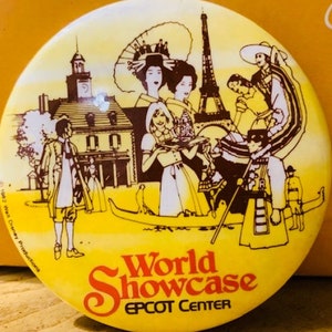 Puede incluir: Un botón amarillo y marrón con una ilustración colorida de personas y monumentos de todo el mundo. El texto "World Showcase EPCOT CENTER" está impreso en el botón.