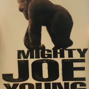 Może przedstawiać: Biały plakat z czerwonym i czarnym tekstem. Plakat przedstawia czarno-białe zdjęcie goryla. Tekst brzmi "Walt Disney Pictures Presents Mighty Joe Young Own It On Video March 23."