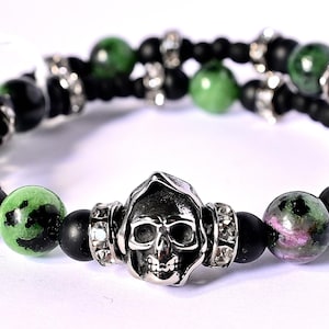 May include: A black and green beaded bracelet with a silver skull charm. The bracelet features black onyx beads, green aventurine beads, and silver spacer beads.