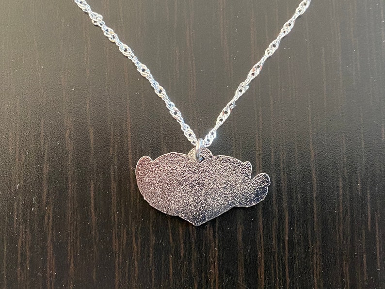 Puede incluir: Un collar de cadena de plata con un colgante de coraz&oacute;n de plata.
