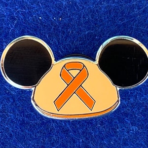 May include: A silver pin shaped like Mickey Mouse's head with an orange ribbon on the front. The ribbon is a symbol of awareness for childhood cancer.