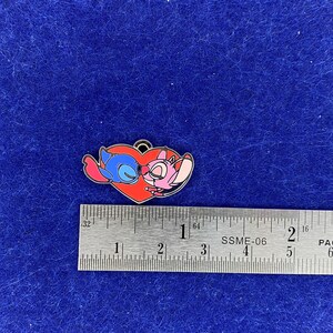 Puede incluir: Un pin en forma de coraz&oacute;n rojo con un Stitch azul y un Angel rosa de la pel&iacute;cula de Disney Lilo & Stitch bes&aacute;ndose. El pin mide aproximadamente 2,5 cm de ancho.
