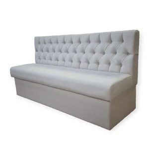 May include: A white upholstered bench with a tufted back and a storage compartment. The bench is designed for use in a restaurant or cafe.
