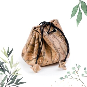 May include: A small, cork-textured drawstring bag with a black cord. The bag is closed and has a natural, earthy look.