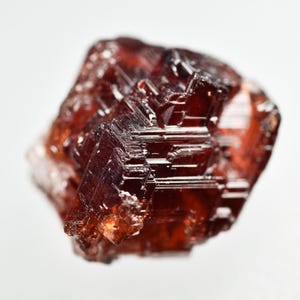 Può includere: Una pietra preziosa di granato sfaccettata di colore rosso intenso con una texture naturale ruvida.