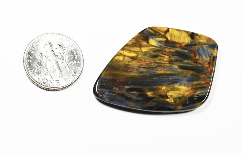 May include: A polished, irregularly shaped gemstone with a mix of gold, blue, and brown hues. The stone is next to a US dime coin for size comparison. The gemstone's surface has a glossy finish and a unique pattern.