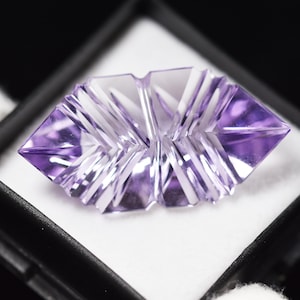 Può includere: Una pietra preziosa di ametista sfaccettata con una tonalità viola, tagliata in una forma a stella unica. La pietra preziosa è esposta in una scatola di velluto nero.