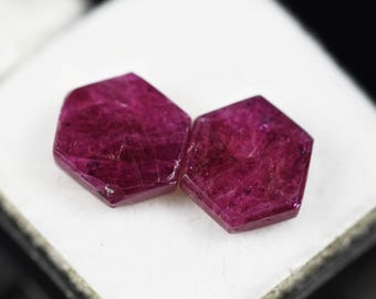 Puede incluir: Dos piedras preciosas sueltas de corte hexagonal con un color rojo magenta profundo y saturado. Las piedras presentan una superficie plana y pulida con inclusiones internas visibles y texturas cristalinas naturales.