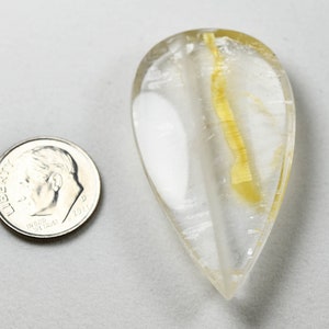 Op de afbeelding: Een traanvormig, helder kwartskristal met een gele insluiting. Het kristal is ongeveer zo groot als een Nederlandse munt van tien cent.