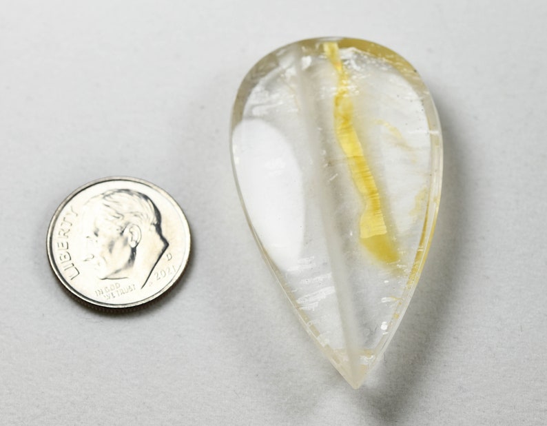 Op de afbeelding: Een traanvormig, helder kwartskristal met een gele insluiting. Het kristal is ongeveer zo groot als een Nederlandse munt van tien cent.