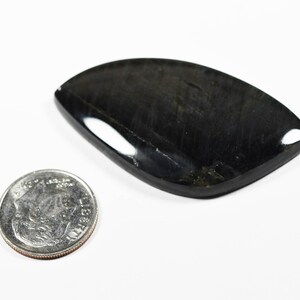 Op de afbeelding: Een gepolijste, traanvormige zwarte edelsteen cabochon met een glad, reflecterend oppervlak. De steen ligt naast een standaard Amerikaanse munt van tien cent, die een diameter van ongeveer 1,8 cm heeft voor de schaal.