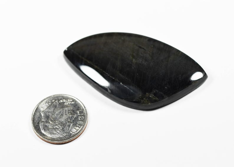 Op de afbeelding: Een gepolijste, traanvormige zwarte edelsteen cabochon met een glad, reflecterend oppervlak. De steen ligt naast een standaard Amerikaanse munt van tien cent, die een diameter van ongeveer 1,8 cm heeft voor de schaal.