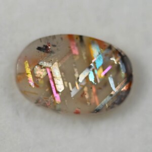 May include: An oval-shaped gemstone with a translucent base, showcasing internal inclusions of various colors. The inclusions appear as iridescent streaks of pink, blue, yellow, and orange, creating a unique, eye-catching pattern. The gemstone has a polished surface.